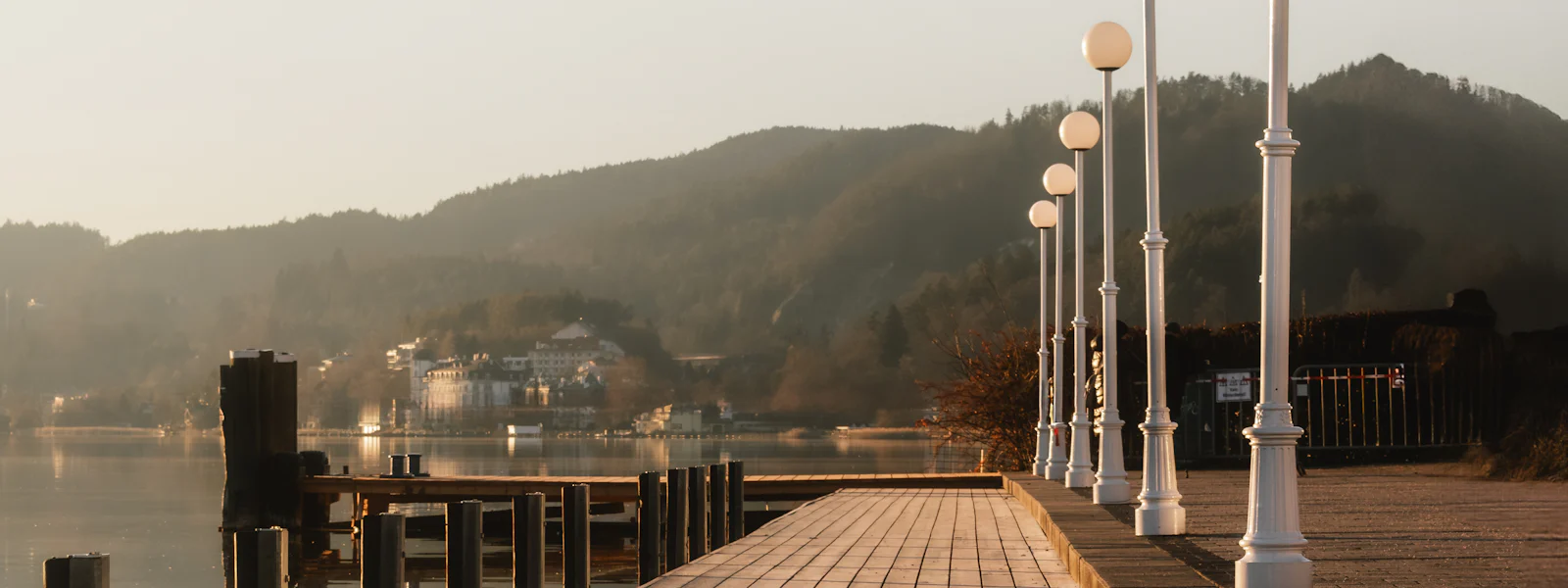A lamp-lined lakeside promenade at first light, mountains behind